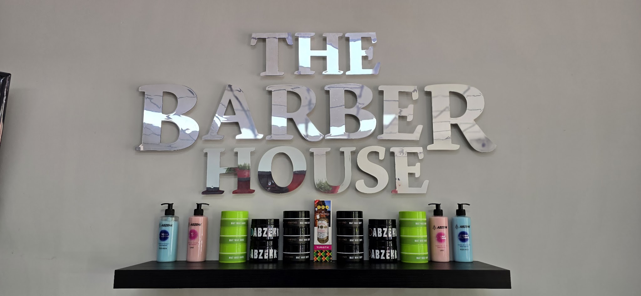 Chromen letters THE BARBER HOUSE aan de muur boven een plank met stylingproducten